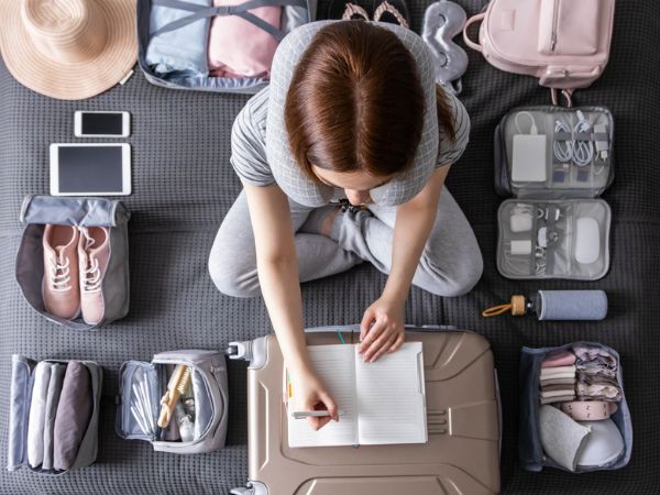 Donna che fa la checklist di viaggio mentre prepara la valigia in vacanza