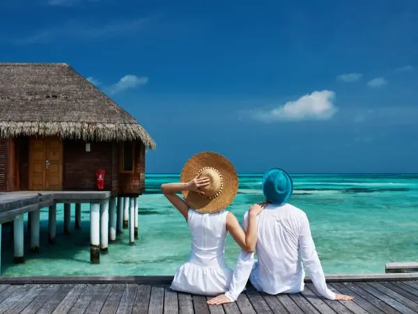 Una coppia in luna di miele alle Maldive, seduta su una spiaggia di sabbia bianca con palme e mare turchese cristallino sullo sfondo, atmosfera romantica al tramonto. Una coppia in luna di miele alle Maldive, seduta su una spiaggia di sabbia bianca con palme e mare turchese cristallino sullo sfondo, atmosfera romantica al tramonto.